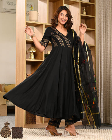 Woman in a black outfit with gold embroidery holding a matching dupatta in a room.