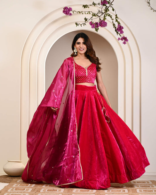 Woman in a vibrant red traditional outfit with a pink dupatta standing in front of an archway.
